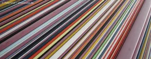Das Bild zeigt viele bunte, parallele Linien in verschiedenen Farben und Breiten, die eine dynamische, abstrakte Optik erzeuge