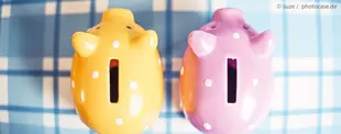 Das Bild zeigt zwei bunte Sparschweine, eines gelb und eines lila mit weißen Punkten, auf einer blau karierten Oberfläche, symbolisch für Sparen und Finanzen.