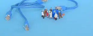 Zwei blaue Netzwerkkabel liegen auf blauem Hintergrund. Dazwischen stehen Miniaturfiguren um eine blaue S-Taste versammelt, als würden sie diskutieren.