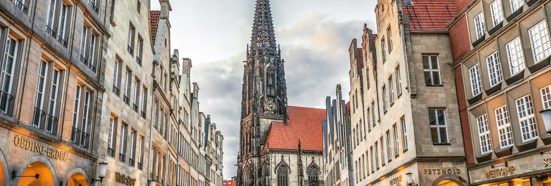 Historischer Prinzipalmarkt in Münster mit der Lambertikirche im Hintergrund, umgeben von traditionellen Giebelhäusern bei stimmungsvollem Licht.