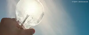 Eine Hand hält eine Glühbirne gegen die Sonne, die durch das Glas strahlt. Symbolisiert Kreativität, Innovation und die Kraft neuer Ideen.