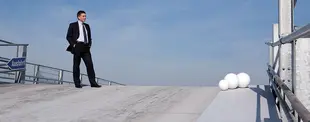 Ein Mann im Anzug steht auf einer leeren Ausfahrt-Rampe, mit weißen Kugeln am Rand und einem klaren Himmel im Hintergrund