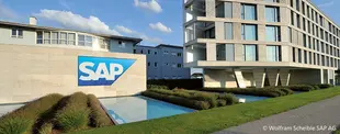 Das Bild zeigt das SAP-Firmengebäude mit einem modernen Glasbau und dem SAP-Logo an einer Wasserfläche, umgeben von Grünanlagen unter blauem Himmel.