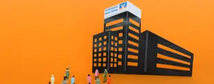 Miniaturfiguren stehen vor einem stilisierten schwarzen Hochhaus mit dem Logo der Volksbank Ruhr Mitte auf orangefarbenem Hintergrund.
