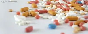 Das Bild zeigt eine Vielzahl bunter Tabletten und Pillen, verstreut auf einer weißen Oberfläche, symbolisch für Medizin, Pharmazie oder Gesundheitsversorgung.