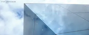 Moderne Glasfassade spiegelt den Himmel, symbolisiert Innovation und Cloud-Technologie. Minimalistisches Design mit klaren Linien und reflektierender Oberfläche.