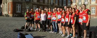ChatGPT:  Eine Gruppe von Läuferinnen und Läufern in roten Noventum-Shirts posiert vor dem Schloss Münster für ein Teamfoto beim Münster-Marathon 2012.