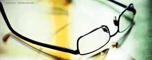 Nahaufnahme einer Brille auf einem Dokument mit warmen Lichtreflexionen, symbolisiert strategisches Denken, Analyse und klare Sicht auf komplexe Zusammenhänge.