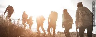 Eine Gruppe Wanderer mit Rucksäcken steigt einen Hügel hinauf, von der Sonne im Gegenlicht beleuchtet.