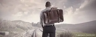 Ein Mann im Anzug mit einer Ledertasche steht auf Bahngleisen und blickt in die Ferne, symbolisierend Aufbruch, Veränderung oder eine ungewisse Zukunft