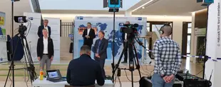 Eine Live-Aufnahme eines Events mit Kamerateam, Moderatoren und Technikern. Im Hintergrund Banner der IHK Nord Westfalen mit Weltkarte und Wirtschaftsthemen.
