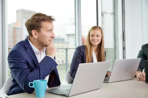 Ein Mann und eine Frau in Business-Kleidung sitzen mit Laptops in einem modernen Büro.