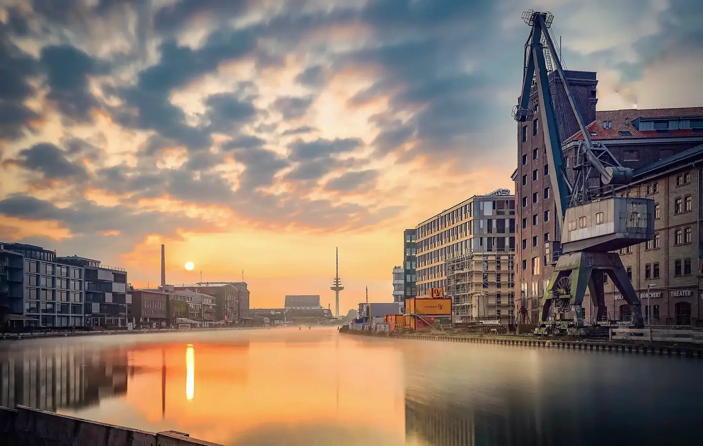 Münsters Hafenviertel bei Sonnenuntergang mit Spiegelung im Wasser, modernen Gebäuden, einem alten Kran und einer lebendigen, historischen Industriearchitektur.
