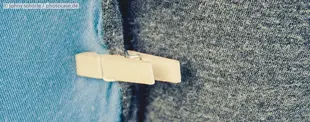 Das Bild zeigt eine hölzerne Wäscheklammer, die zwei unterschiedlich farbige Stoffe, einen blauen und einen grauen, zusammenhält. Nahaufnahme mit Texturdetails.