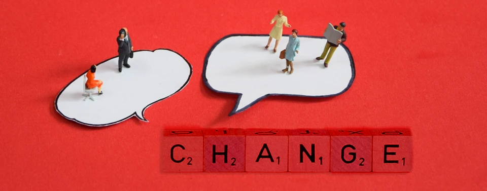 Das Bild zeigt Miniaturfiguren in Sprechblasen über roten Scrabble-Steinen, die das Wort „CHANGE“ bilden.