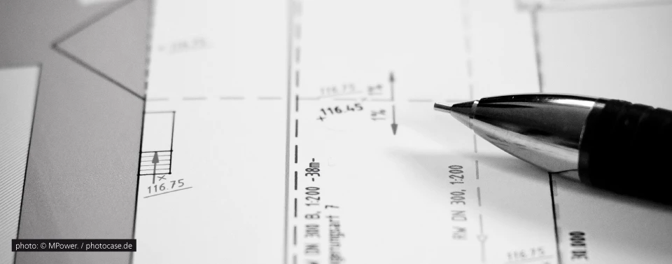 Ein technischer Bauplan in Schwarz-Weiß mit Maßangaben. Ein Druckbleistift liegt darauf, bereit für Notizen oder Anpassungen.