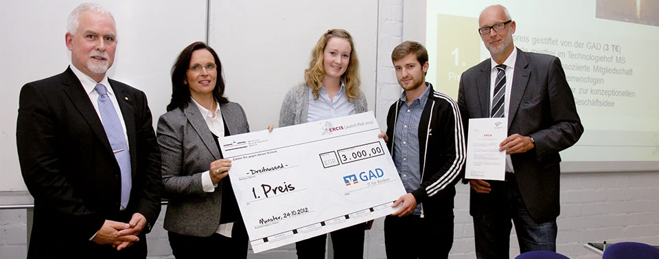 Fünf Personen stehen in einem Raum, zwei halten einen übergroßen Scheck für den 1. Preis des ERCIS Launch Pad 2012, gestiftet von der GAD.