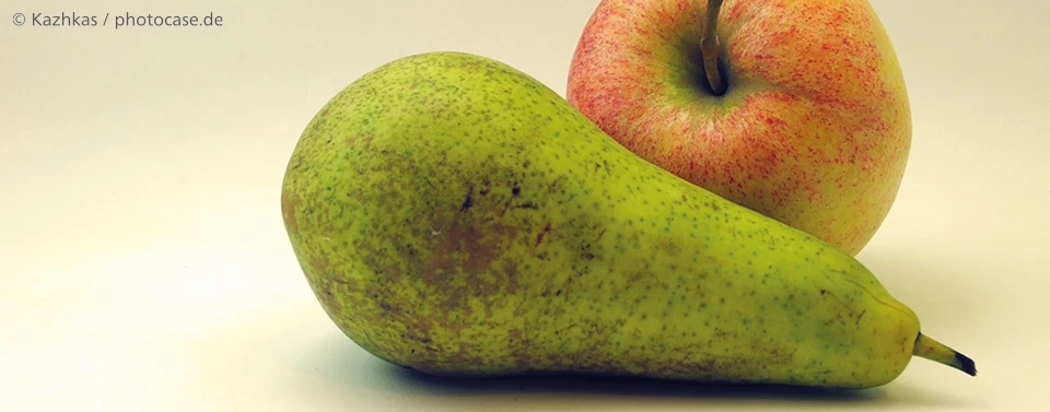 Das Bild zeigt eine grüne Birne im Vordergrund und einen roten Apfel im Hintergrund auf einer neutralen Oberfläche.