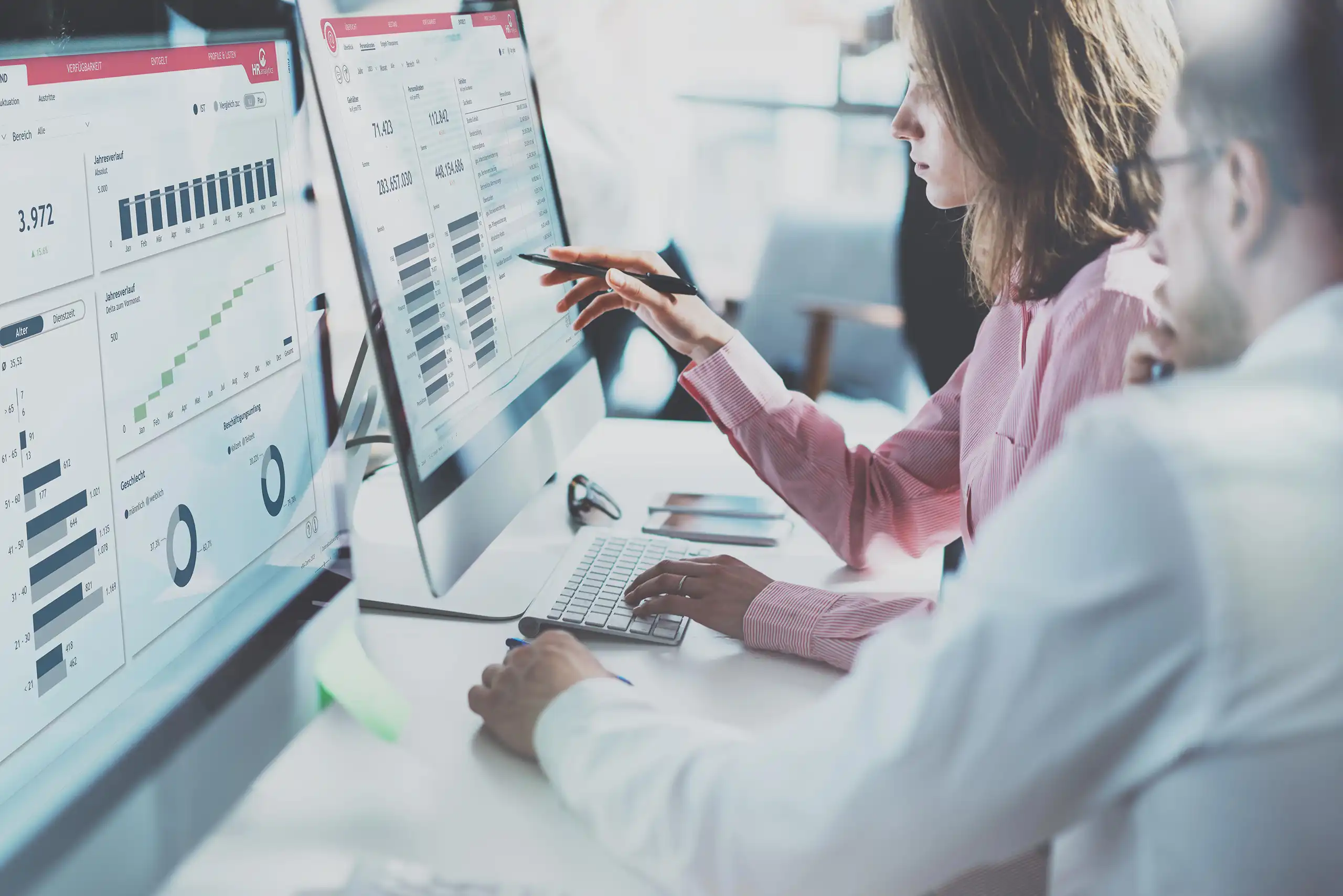Zwei Personen analysieren HR-Analytics-Daten auf großen Monitoren in einem modernen Büro.