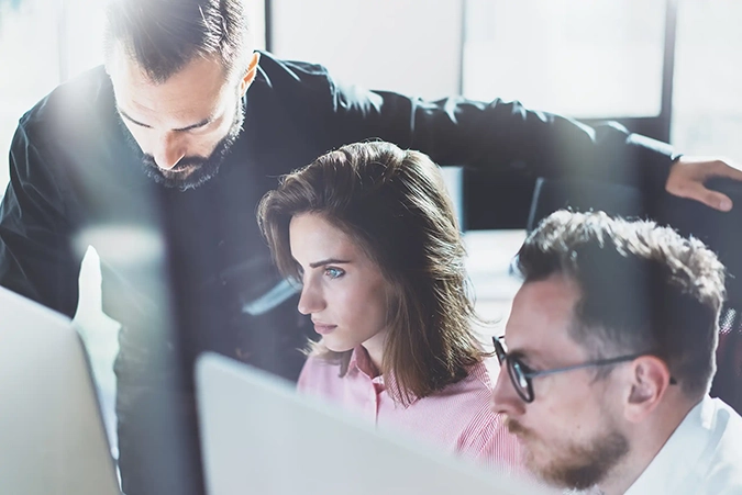 Drei Personen analysieren konzentriert Daten auf einem Bildschirm in einem modernen Büro.