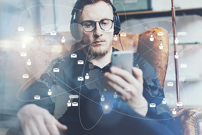 Ein Mann mit Kopfhörern schaut auf sein Smartphone. Überlagert ist er durch eine digitale Weltkarte mit Icons für Kommunikation und Vernetzung.