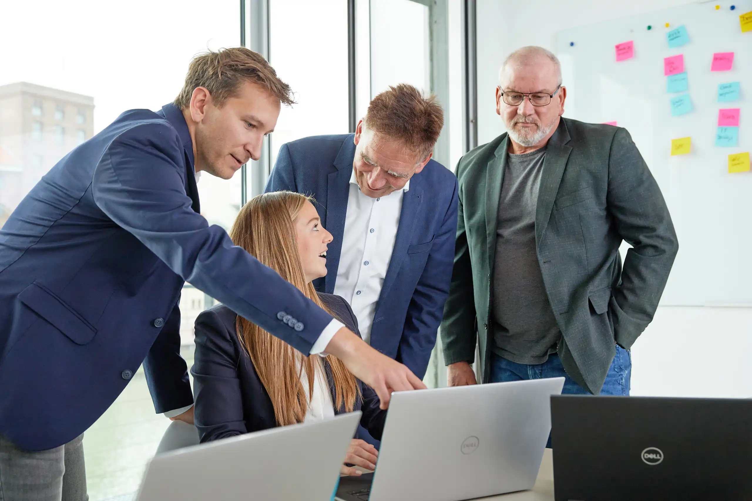 Vier Geschäftsleute in einem modernen Büro besprechen ein Projekt. Ein Mann zeigt auf den Laptop einer Kollegin, während die anderen aufmerksam zuhören.